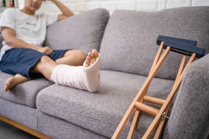 Man with broken leg in cast sitting on couch with crutches after a car accident in Brooklyn New York — personal injury pain and suffering claim