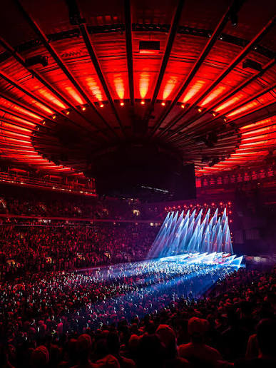 Sold-out crowd inside Madison Square Garden under red lighting during a concert, with blue stage lights illuminating the stage