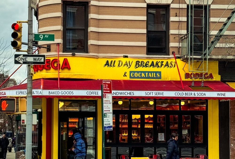 Bright yellow bodega on 9th Avenue corner in New York City advertising all-day breakfast and cocktails