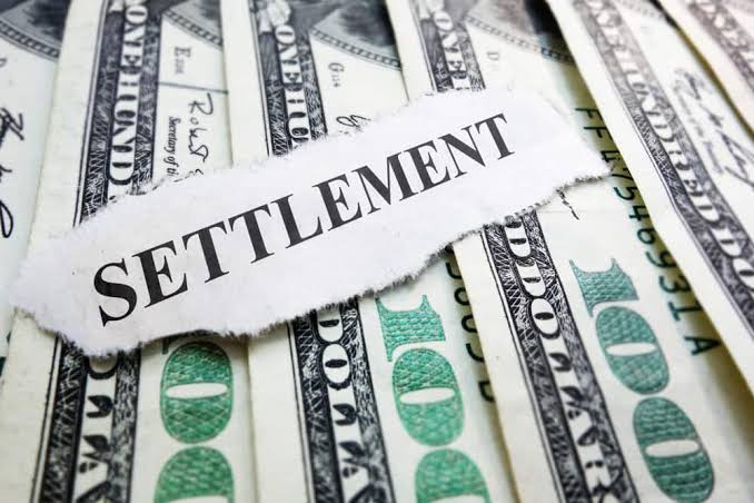 Torn paper strip reading "Settlement" resting on a spread of hundred-dollar bills