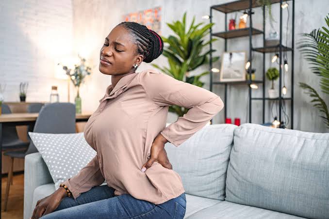Home health aide in Brooklyn holding her lower back in pain from a work injury caused by lifting and transferring patients