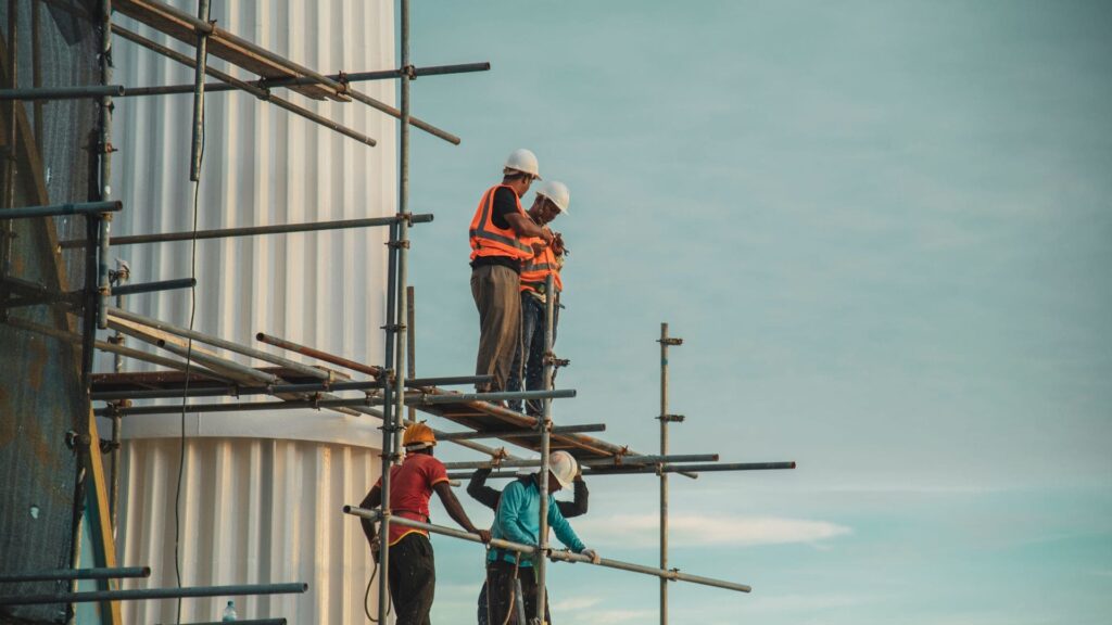 Construction workers in hard hats standing on high scaffolding without guardrails, the kind of fall risk New York’s Scaffold Law protects every worker against, with or without papers
