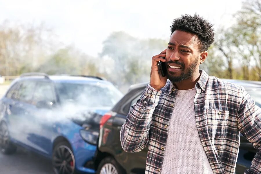 Upset driver calls for help on his phone beside two crashed cars, the first step after being hit by an uninsured driver in NYC